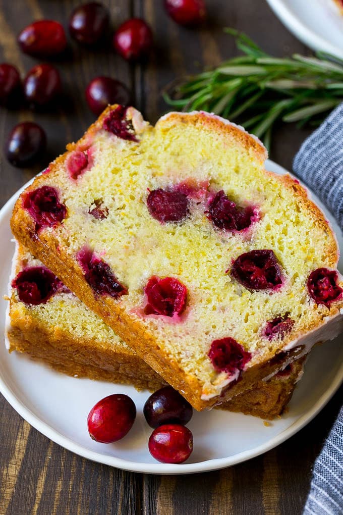 Cranberry Bread Recipe | Cranberry Loaf | Cranberry Orange Bread #cranberry #bread #baking #dessert #fall #edsug A plate with two slices of cranberry bread and fresh cranberries for garnish.