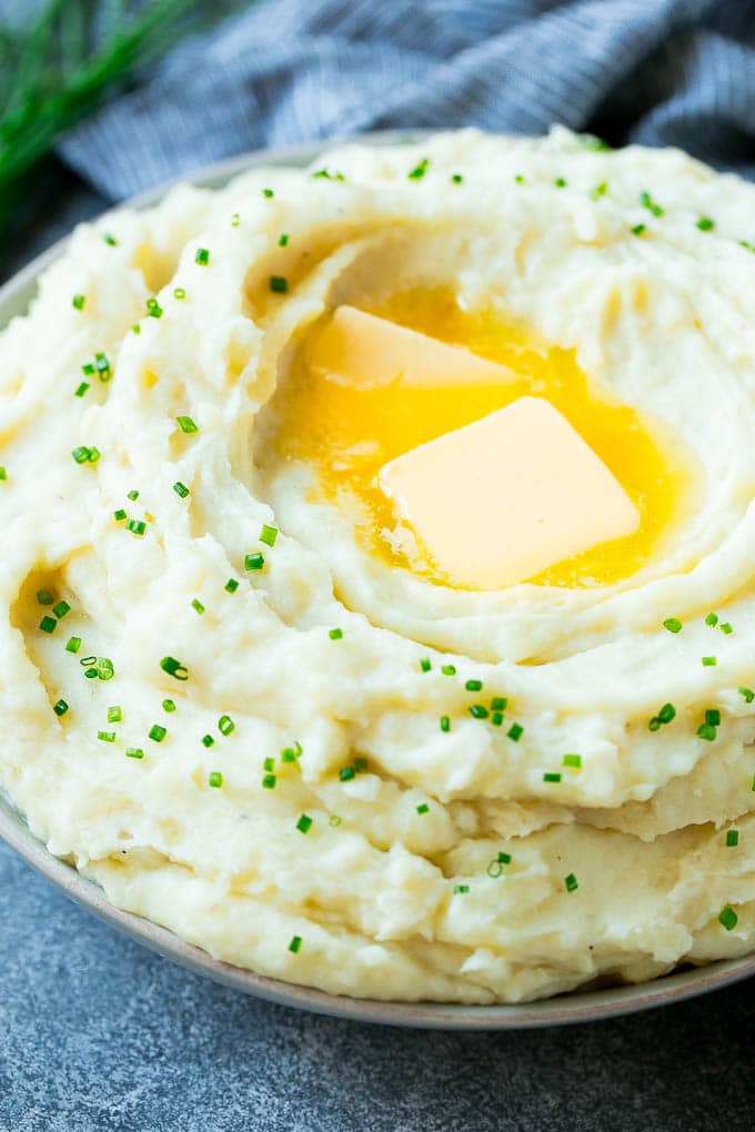Instant Pot Mashed Potatoes Recipe | Pressure Cooker Mashed Potatoes | Easy Mashed Potatoes #potatoes #sidedish #instantpot #thanksgiving #dinner #edsug A bowl of fluffy Instant Pot mashed potatoes topped with pats of butter and sliced chives.