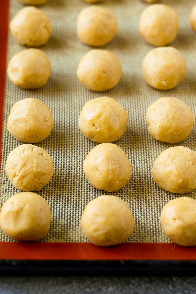 Peanut Butter Blossoms Recipe | Hershey Kiss Cookies | Chocolate Peanut Butter Cookies #cookies #peanutbutter #chocolate #dessert #baking #christmas #christmascookies #edsug Balls of dough on a baking sheet.