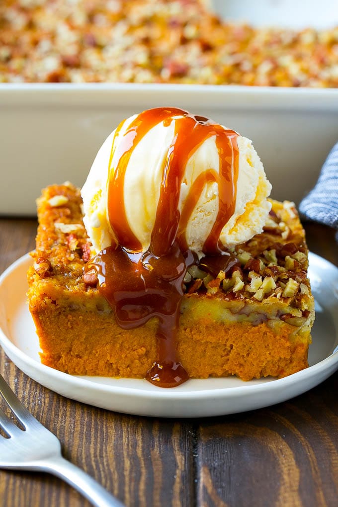 Pumpkin Dump Cake Recipe | Pumpkin Cake | Pumpkin Pie Cake #pumpkin #cake #pecans #fall #thanksgiving #dessert #edsug A slice of pumpkin dump cake topped with ice cream and caramel sauce.