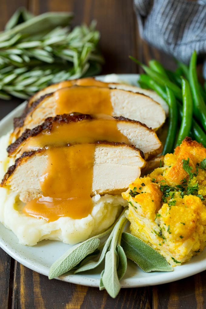 This slow cooker turkey breast is coated in a seasoned herb butter, then placed in the crock pot to cook to tender perfection. It's the perfect way to free up oven space for your big holiday meal. Sliced slow cooker turkey breast served with stuffing and green beans.