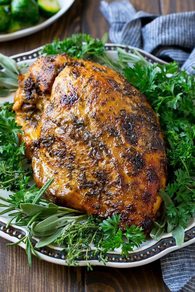 This slow cooker turkey breast is coated in a seasoned herb butter, then placed in the crock pot to cook to tender perfection. It's the perfect way to free up oven space for your big holiday meal. A slow cooker turkey breast on a serving platter with fresh herbs.