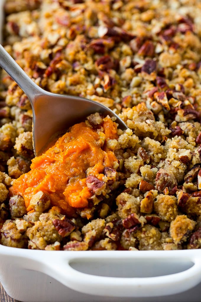 Sweet Potato Casserole with Pecans Recipe | Sweet Potato Casserole | Sweet Potato Side Dish #sweetpotatoes #thanksgiving #pecans #casserole #sidedish #holiday #fall #edsug A dish of sweet potato casserole with pecans with a serving spoon in it.