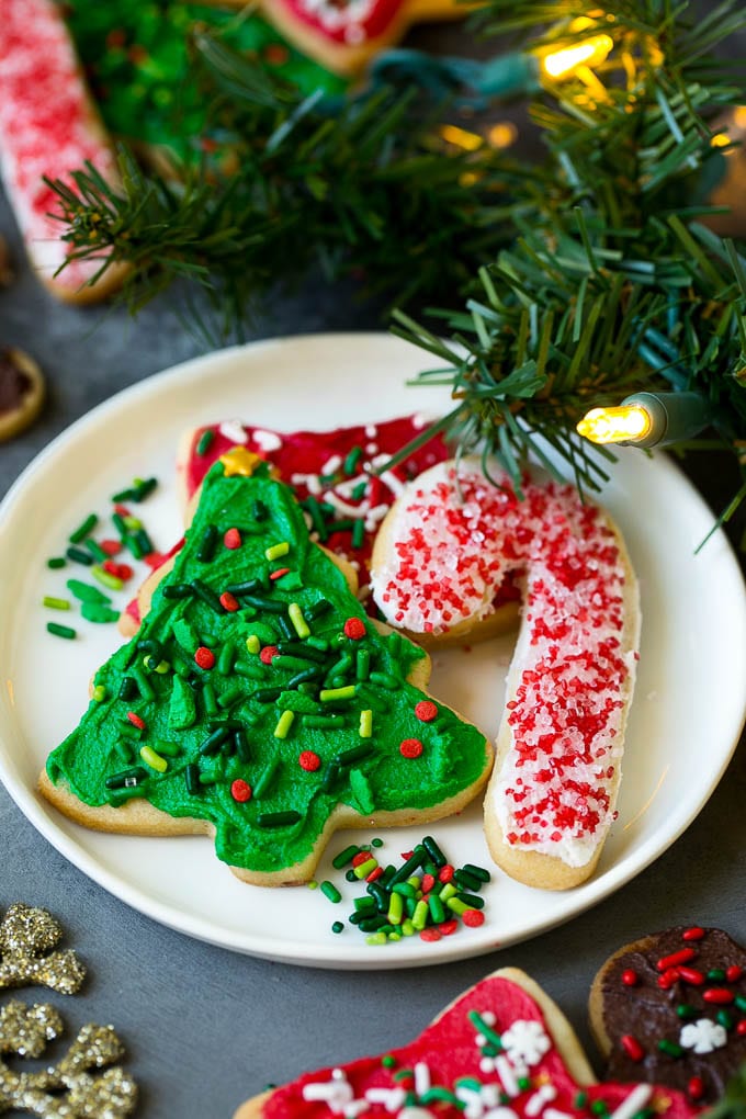 Christmas Sugar Cookies Recipe | Christmas Cookies #cookies #frosting #sprinkles #sugarcookies #christmas #dessert #edsug A selection of Christmas sugar cookies served on a plate, with holiday decorations in the background.
