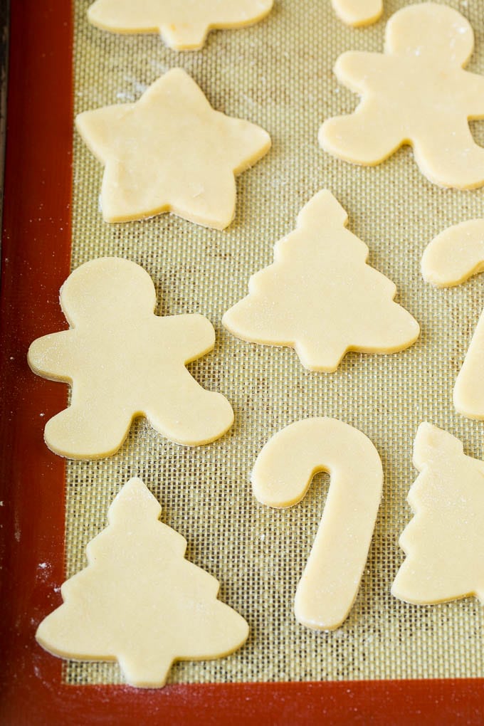 Christmas Sugar Cookies Recipe | Christmas Cookies #cookies #frosting #sprinkles #sugarcookies #christmas #dessert #edsug Cookie dough cut into holiday shapes on a baking sheet.