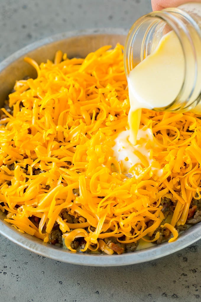 Cheeseburger Pie Recipe | Cheeseburger Casserole | Ground Beef Recipe #cheeseburger #beef #bacon #cheese #casserole #dinner #edsug Egg batter being poured over shredded cheese and ground beef.