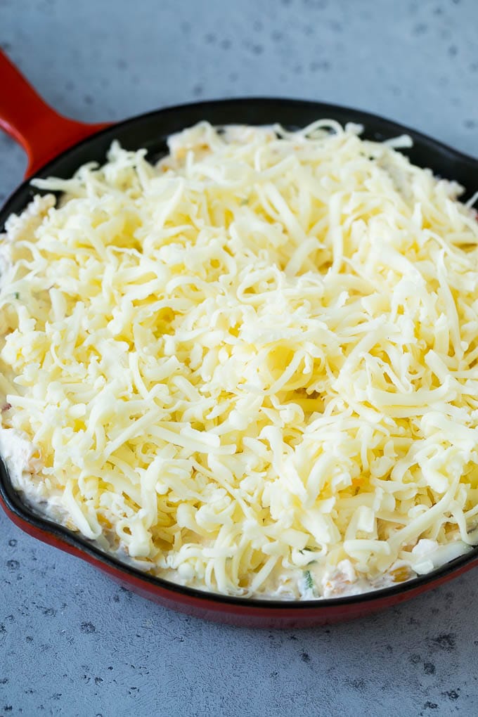 Corn Dip Recipe | Hot Cheese Dip | Bacon Dip #corn #dip #bacon #cheese #appetizer #snack #edsug A skillet of corn dip covered with shredded cheese.