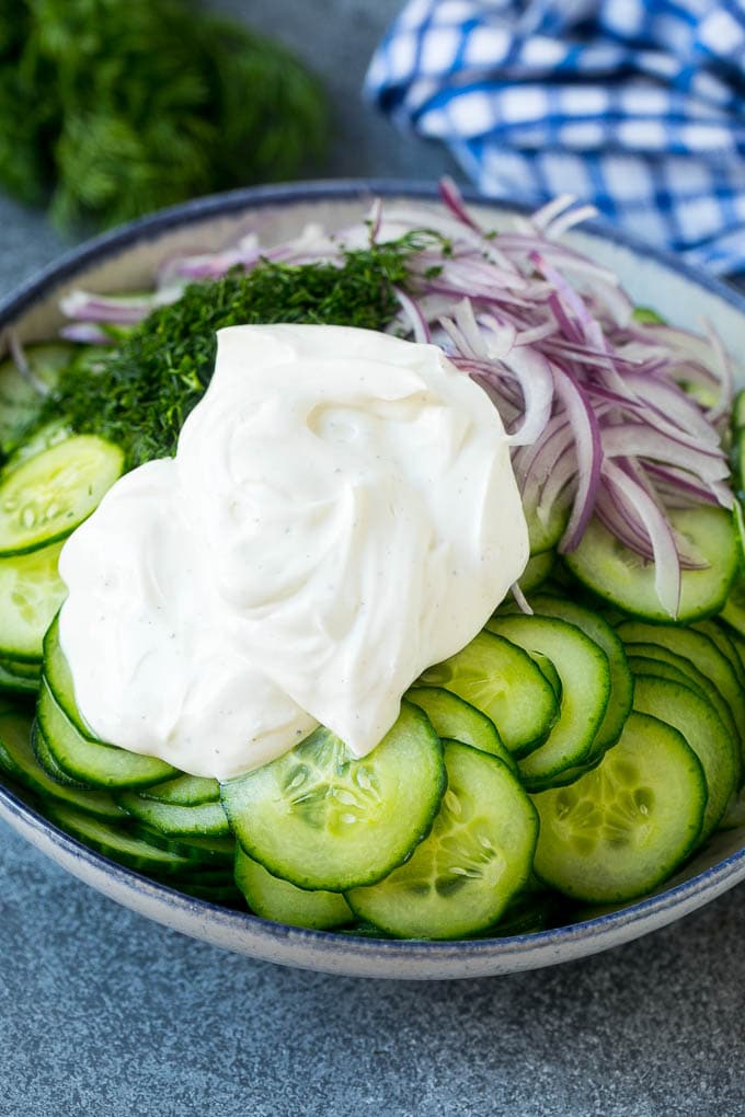 Creamy Cucumber Salad Recipe | German Cucumber Salad | Cucumber Salad #cucumber #salad #dinner #lunch #edsug #cucumbersalad Cucumbers, red onion and dill in a bowl topped with creamy dressing.