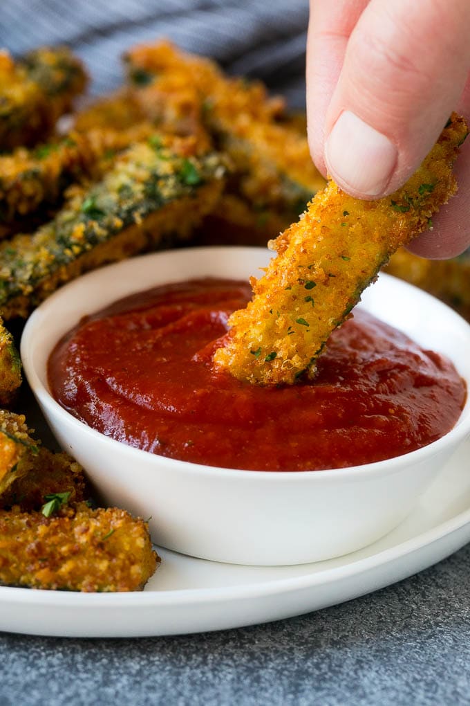 Fried Zucchini Recipe | Zucchini Fries | Zucchini Recipe #appetizer #zucchini #snack #edsug A hand dipping a piece of fried zucchini into marinara sauce.
