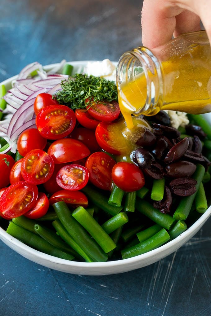 Green Bean Salad Recipe | String Bean Salad | Chopped Salad #greenbeans #tomatoes #olives #salad #cleaneating #lowcarb #glutenfree #edsug Dressing being poured over veggies like cherry tomatoes, olives and onions.
