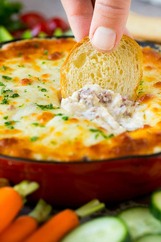 Reuben Dip Recipe | Corned Beef Dip | Cheese Dip #dip #cheese #cornedbeef #appetizer #lowcarb #keto #edsug A baguette chip dipping into a skillet of Reuben dip.