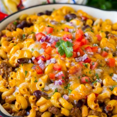 A skillet of chili mac topped with melted cheese, diced tomatoes and minced onion.