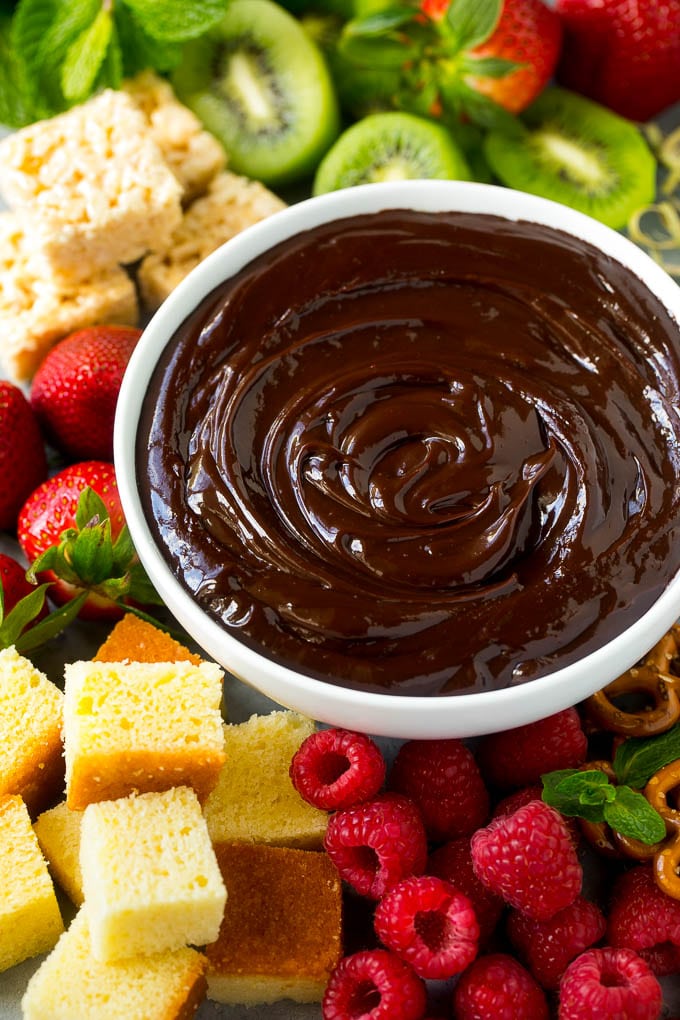 Chocolate Fondue Recipe | Chocolate Sauce | Chocolate Dip #chocolate #dessert #glutenfree #fondue #edsug A bowl of chocolate fondue surrounded by fruit, cake, rice krispy treats and pretzels.