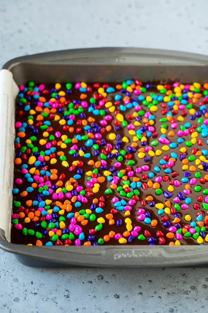 Cosmic Brownies Recipe | Cocoa Brownies | Frosted Brownies #brownies #chocolate #dessert #edsug #sprinkles A pan of cosmic brownies with rainbow sprinkles on top.