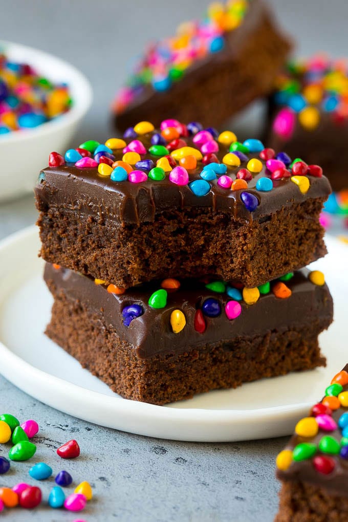 Cosmic Brownies Recipe | Cocoa Brownies | Frosted Brownies #brownies #chocolate #dessert #edsug #sprinkles A stack of cosmic brownies on a plate with a bite taken out of one.