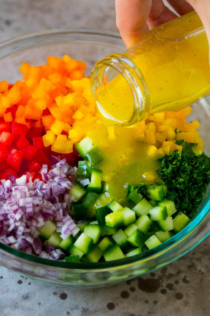 Israeli Salad Recipe | Cucumber Salad | Tomato Salad | Chopped Salad #salad #cleaneating #healthy #glutenfree #lowcarb #keto #sidedish #lunch #edsug Lemon dressing being poured over chopped vegetables.