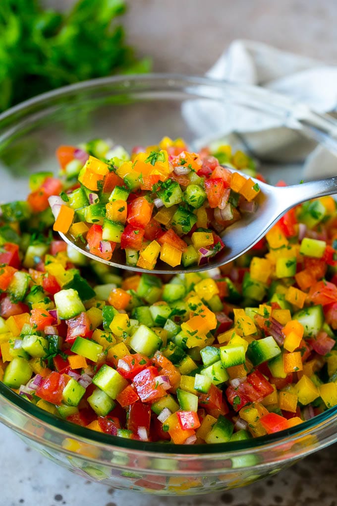 Israeli Salad Recipe | Cucumber Salad | Tomato Salad | Chopped Salad #salad #cleaneating #healthy #glutenfree #lowcarb #keto #sidedish #lunch #edsug A spoon holding up a serving of Israeli salad.