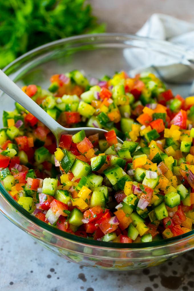 Israeli Salad Recipe | Cucumber Salad | Tomato Salad | Chopped Salad #salad #cleaneating #healthy #glutenfree #lowcarb #keto #sidedish #lunch #edsug A bowl of Israeli salad with a serving spoon in it.