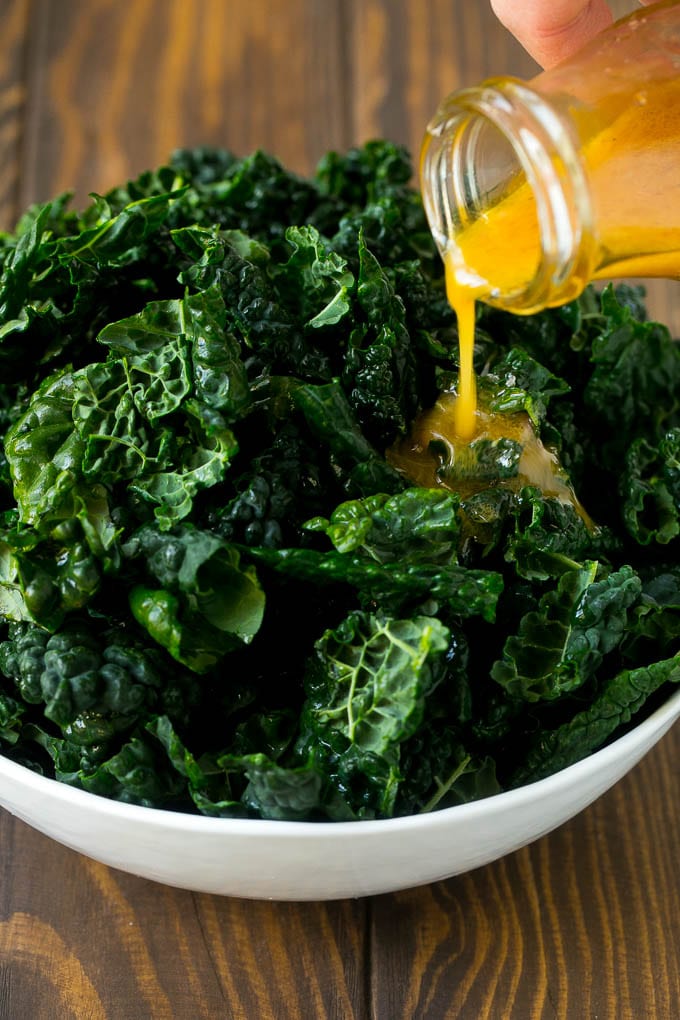 Apple Kale Salad Recipe | Kale Recipe | Fall Salad #kale #apples #bacon #salad #feta #dinner #lunch #edsug Dressing being poured over dinosaur kale leaves.