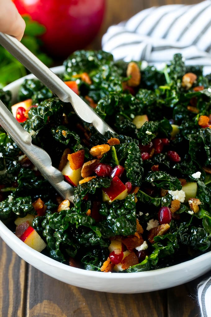Apple Kale Salad Recipe | Kale Recipe | Fall Salad #kale #apples #bacon #salad #feta #dinner #lunch #edsug Tongs in a bowl of kale and apple salad.