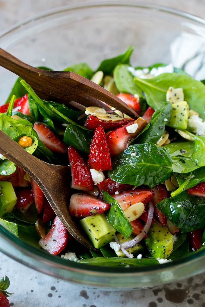 Strawberry Spinach Salad Recipe | Strawberry Salad | Spinach Salad #spinach #salad #strawberries #avocado #edsug Salad tongs in a bowl of spinach salad with strawberries.