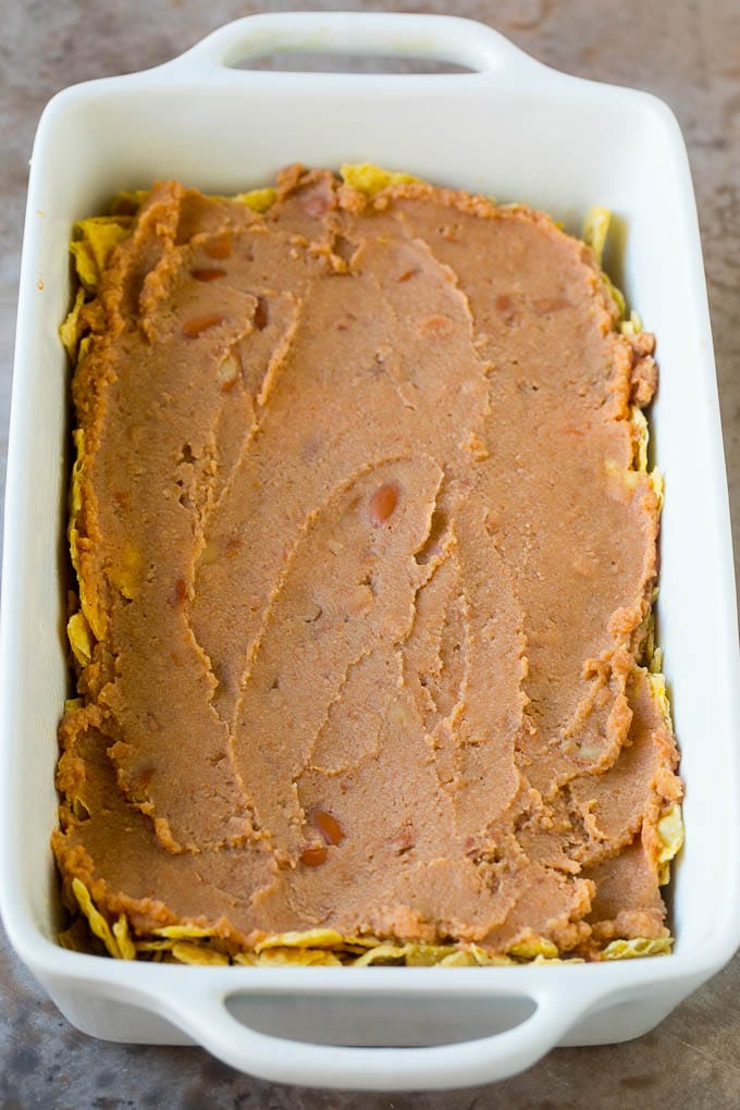Taco Casserole Recipe | Mexican Casserole | Beef Casserole #casserole #tacos #beef #dinner #cheese #edsug A layer of refried beans on top of a crushed tortilla chips.