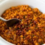 Crock pot baked beans with bacon, with a serving spoon in the pot.