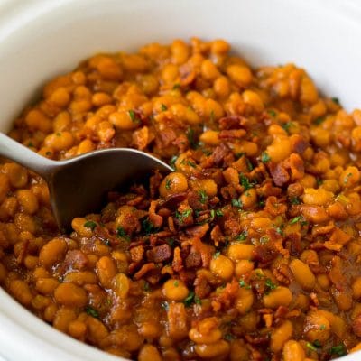 Crock pot baked beans with bacon, with a serving spoon in the pot.