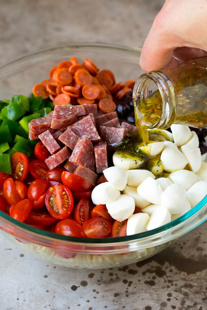 Italian Pasta Salad | Pasta Salad Recipe #pasta #salad #pastasalad #pepperoni #salami #olives #cheese #sidedish #edsug Italian dressing being poured over pasta salad ingredients.