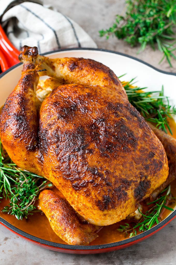 Rotisserie Chicken Recipe | Roasted Chicken #chicken #dinner #edsug #comfortfood A rotisserie chicken in a red skillet with sprigs of fresh herbs.