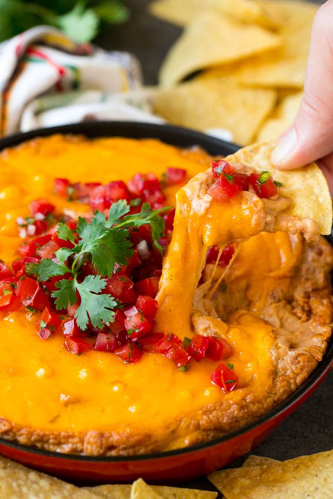 Bean Dip Recipe | Mexican Dip #dip #appetizer #mexicanfood #beans #cheese #edsug A tortilla chip scooping out a serving of Mexican bean dip.