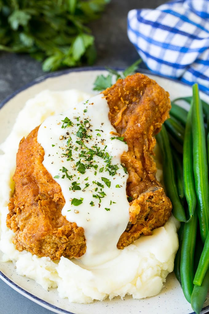A fried pork chop served over mashed potatoes with green beans.