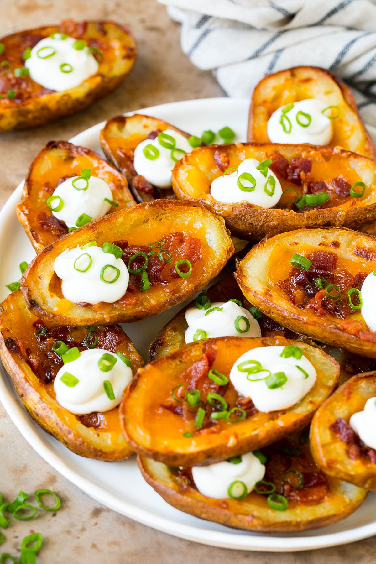 Potato Skins Recipe | Loaded Potatoes #potatoes #appetizer #snack #cheese #bacon #edsug A serving plate of potato skins topped with bacon and sour cream.