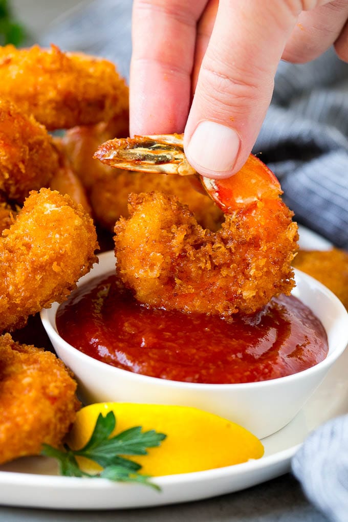 Fried Shrimp Recipe #shrimp #seafood #dinner #appetizer #edsug A hand dipping a shrimp into cocktail sauce.