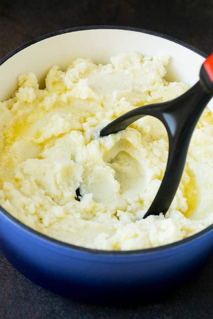 Garlic Mashed Potatoes Recipe #garlic #potatoes #mashedpotatoes #sidedish #dinner #thanksgiving #edsug A potato masher smashing diced cooked potatoes.
