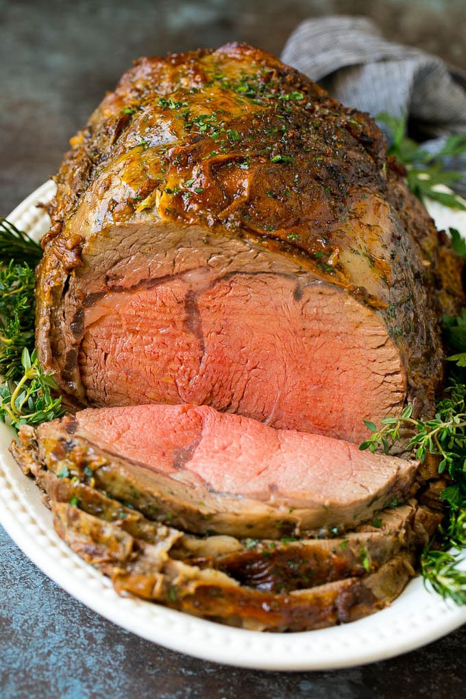 Prime Rib Recipe #primerib #beef #roast #dinner #thanksgiving #christmas #keto #lowcarb #edsug A sliced slow roasted prime rib roast surrounded by fresh herbs.