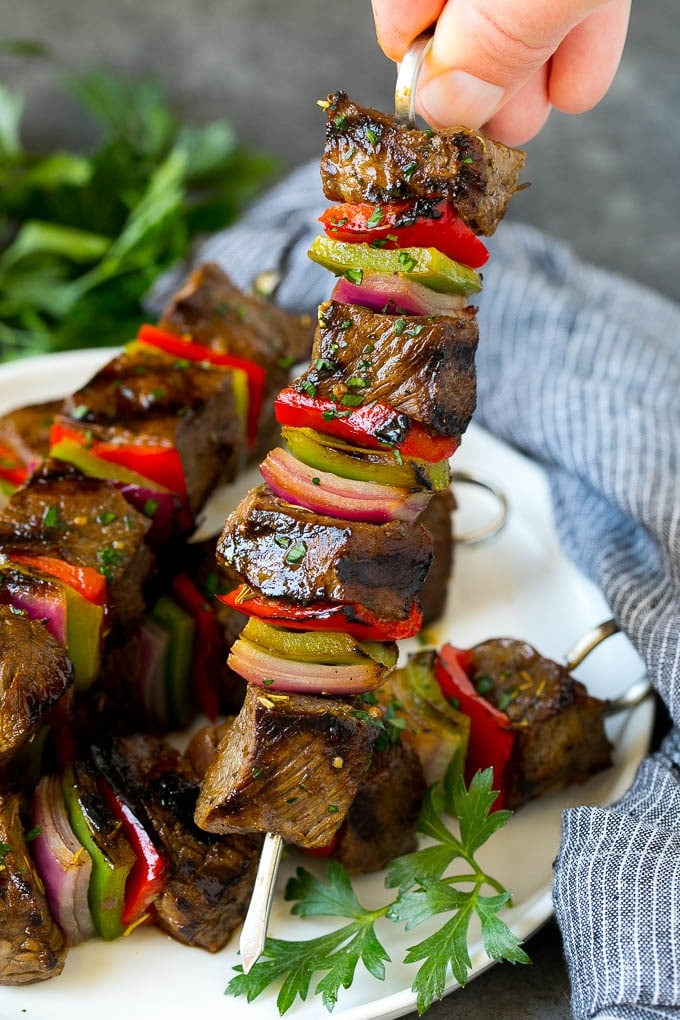 Beef Shish Kabobs Recipe | Beef Kabobs #grilling #beef #steak #dinner #edsug #peppers A hand holding a beef shish kabob with peppers and onions.