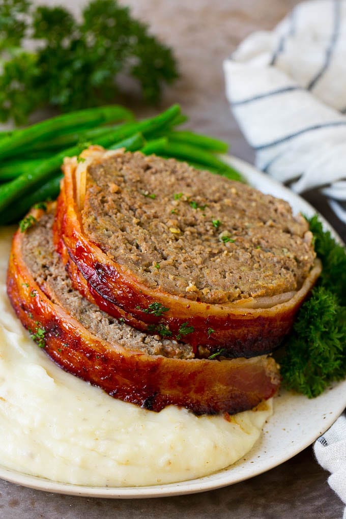 Bacon Wrapped Meatloaf Recipe | Beef Meatloaf #meatloaf #beef #groundbeef #bacon #dinner #edsug Slices of bacon wrapped meatloaf served over mashed potatoes with green beans.