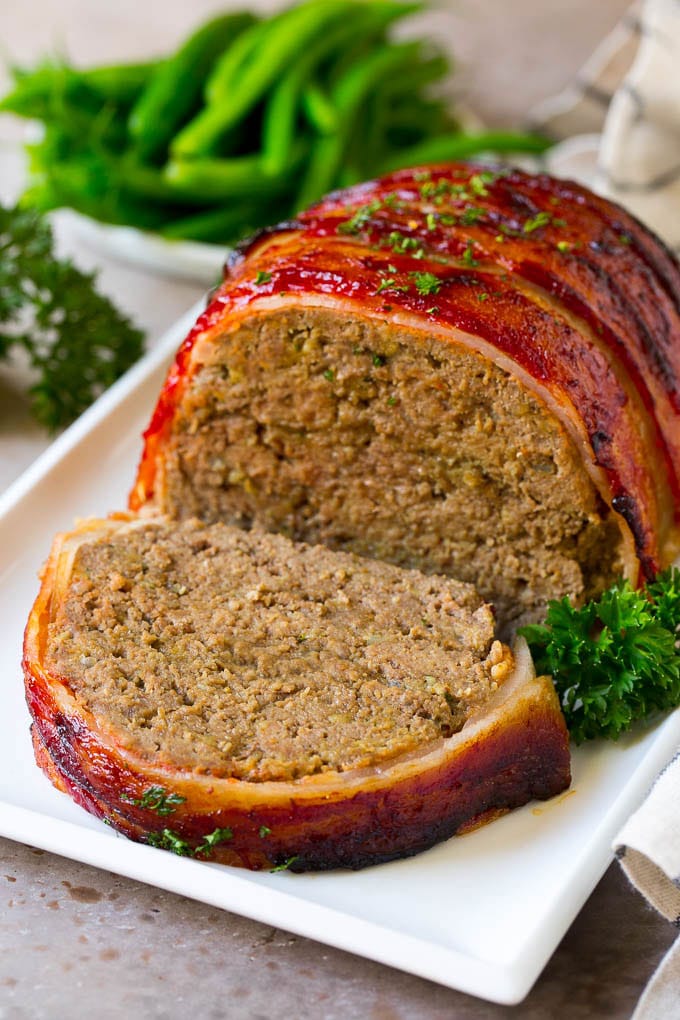 Bacon Wrapped Meatloaf Recipe | Beef Meatloaf #meatloaf #beef #groundbeef #bacon #dinner #edsug A bacon wrapped meatloaf with a slice out of it, on a serving platter.