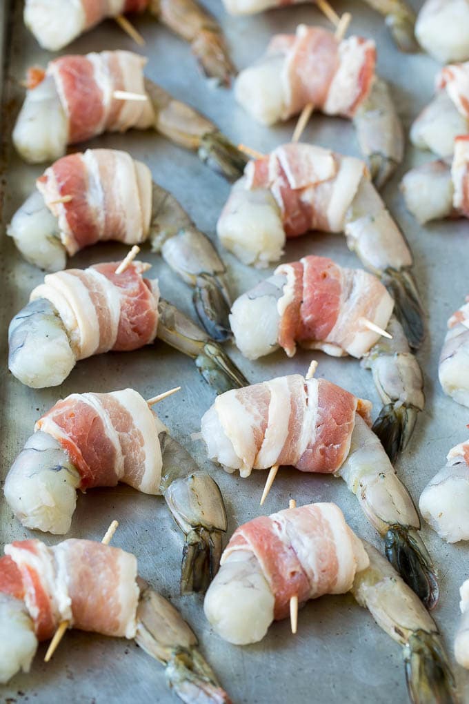 Bacon Wrapped Shrimp Recipe | Bacon Shrimp #shrimp #bacon #appetizer #dinner #edsug #seafood Raw seafood on a sheet pan wrapped in pork.