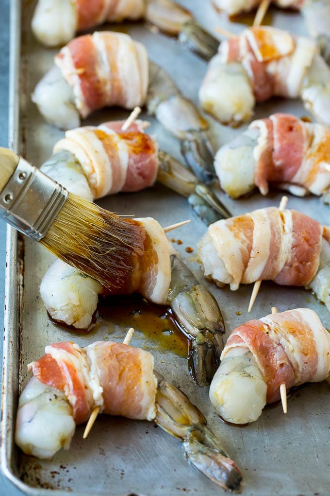 Bacon Wrapped Shrimp Recipe | Bacon Shrimp #shrimp #bacon #appetizer #dinner #edsug #seafood A basting brush applying sauce to shrimp.