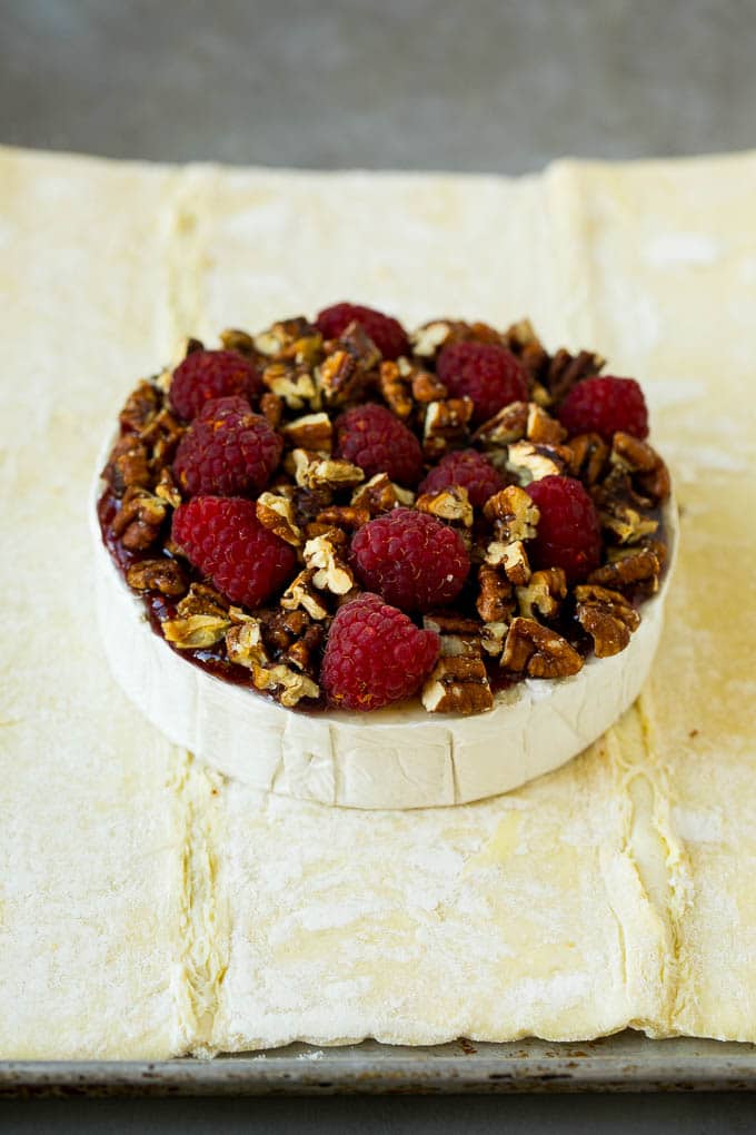 Baked Brie Recipe | Pastry Wrapped Brie #brie #cheese #appetizer #pecans #raspberries #edsug A wheel of cheese topped with jam, raspberries and pecans.