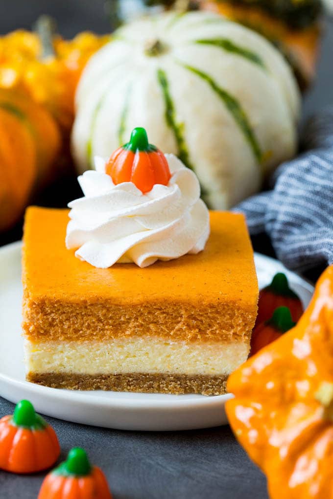These pumpkin cheesecake bars are layers of graham cracker crust, vanilla cheesecake and pumpkin cheesecake, all baked together to create an impressive dessert. Pumpkin cheesecake bars garnished with whipped cream.
