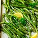 A pan of roasted green beans garnished with parsley and lemon.