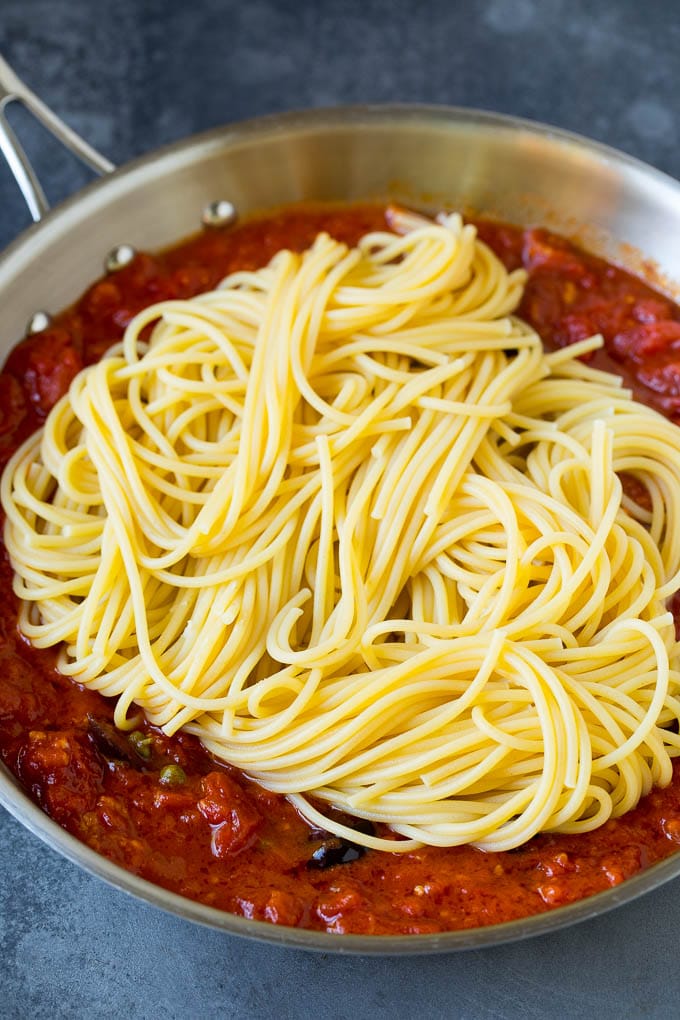 Pasta Puttanesca Recipe #pasta #tomatoes #olives #italianfood #dinner #edsug Spaghetti in a pan of tomato sauce with olives and capers.