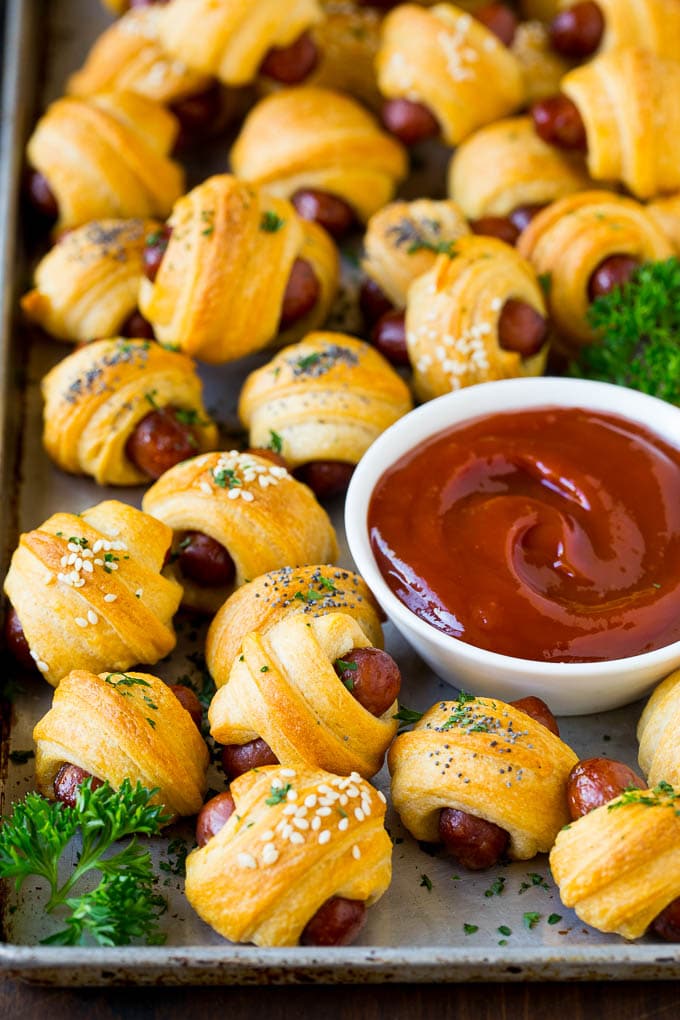 Pigs in a Blanket Recipe #hotdogs #appetizer #snack #comfortfood #edsug A sheet pan of pigs in a blanket, garnished with parsley and served with ketchup.