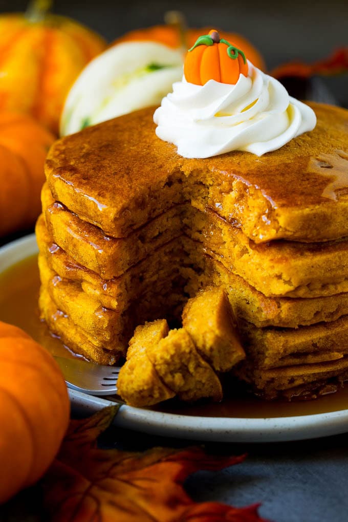 These pumpkin pancakes are light and fluffy buttermilk hotcakes flavored with pumpkin puree and spices. A stack of pumpkin pancakes with a fork holding cut pieces of pancake.