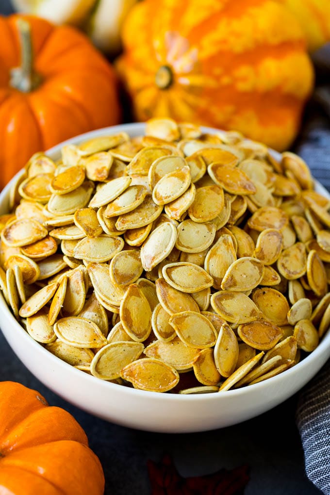 These roasted pumpkin seeds are coated in butter and seasonings, then baked until golden brown. A bowl of roasted pumpkin seeds surrounded by pumpkins and gourds.