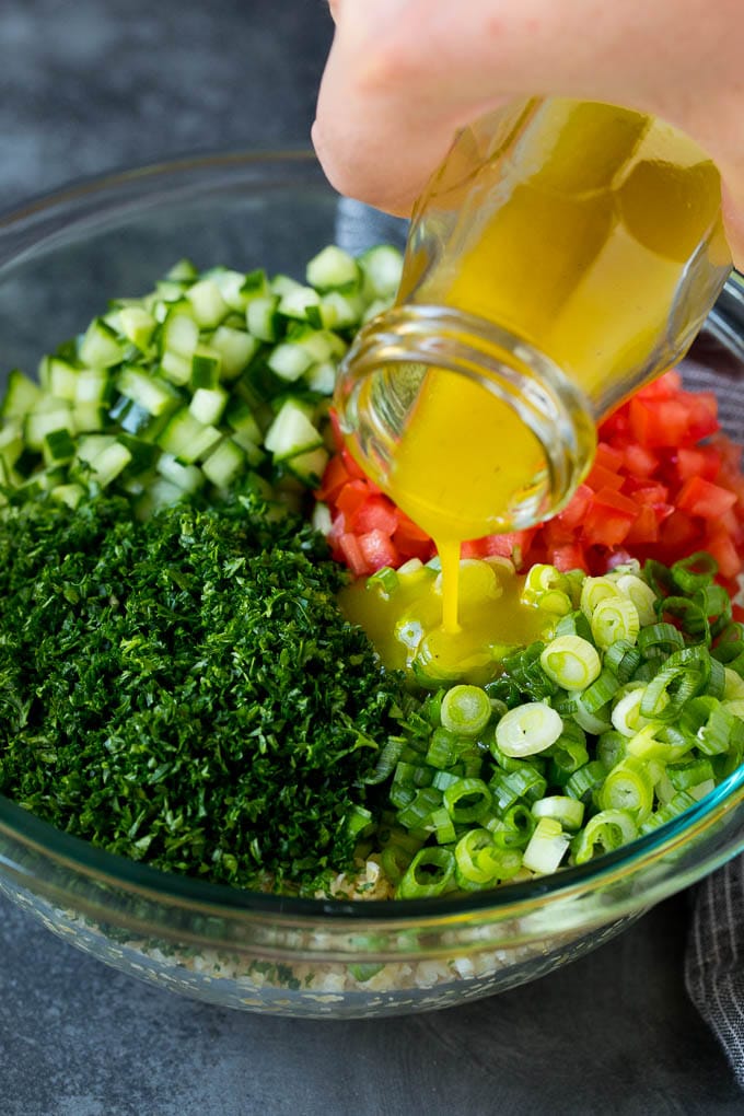 Tabbouleh Salad | Tabouli #salad #wheat #tomatoes #cucumber #healthy #sidedish #dinner #edsug Dressing being poured into a bowl of bulgur wheat salad.
