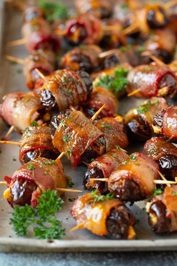 Bacon Wrapped Dates #appetizer #bacon #dates #cheese #edsug Bacon wrapped dates on a sheet pan garnished with parsley.